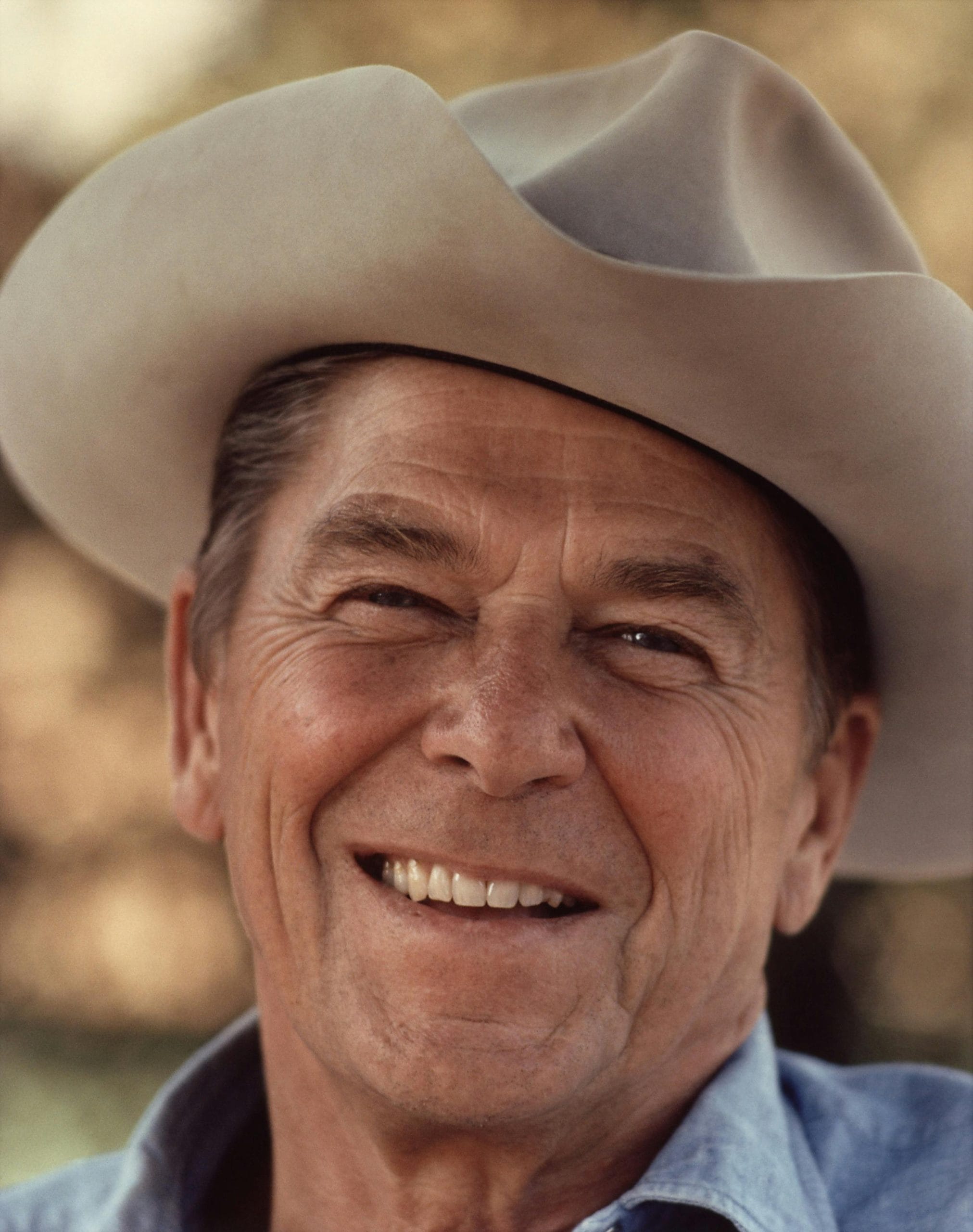 Home 7 Portrait of a senior man wearing a cowboy hat, smiling warmly outdoors.